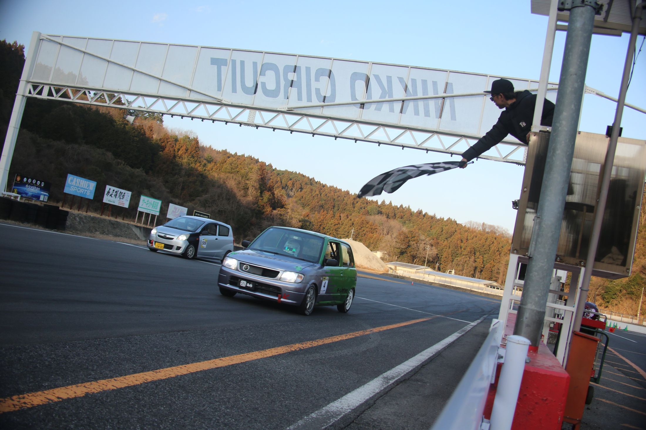 日光サーキットのコントロールラインで、振られるチェッカーフラッグを受けてフィニッシュする軽自動車